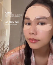Ohra Lifted Forehead Mask as seen on, reusable, medical-grade silicone, Australia. Girl smiling in a selfie with reusable masks on. A woman wearing peach-colored eye mask patches under her eyes and on her forehead, wearing a pink patterned pajama top. Text overlays on the left read 'OHRA LIFTED FOREHEAD MASK SELF MADE EYE MASK' and 'AS SEEN ON @EMLOVESUSHII'.