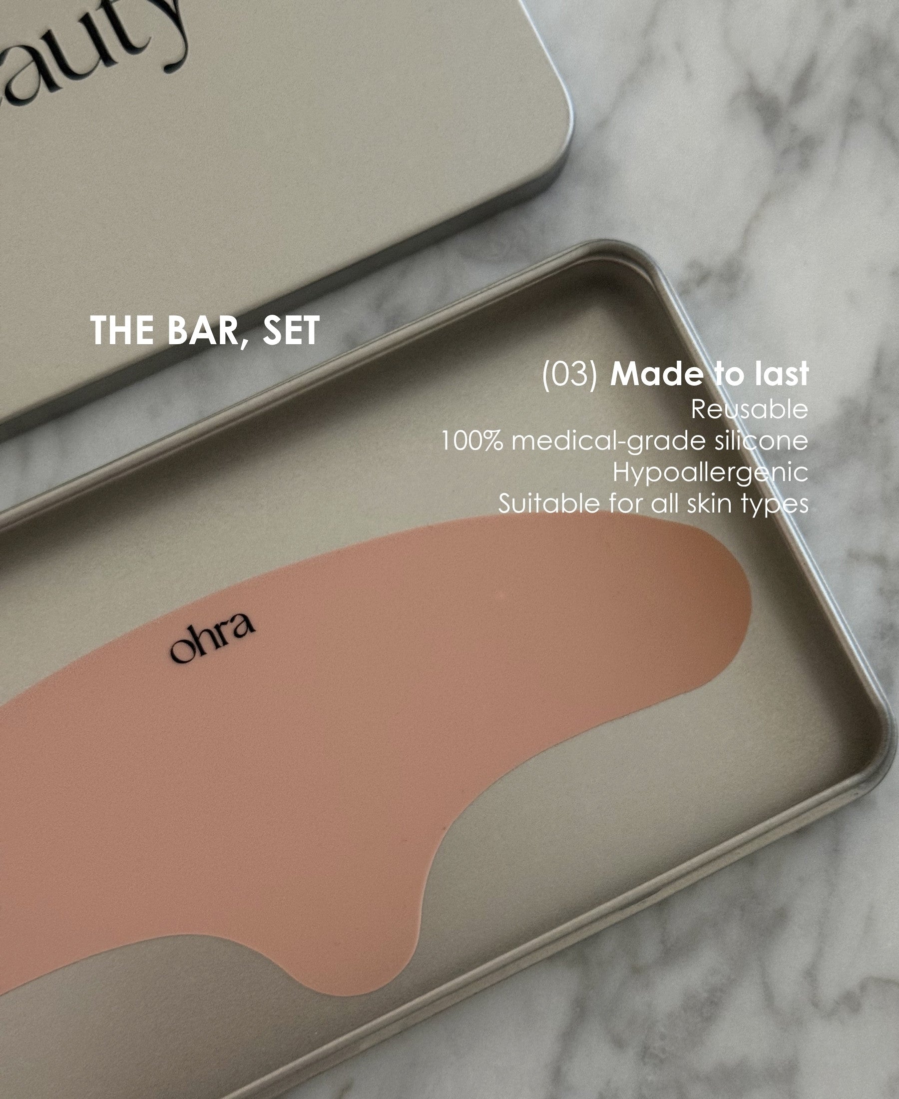 Ohra Lifted Forehead Mask on marble surface, reusable, 100% medical-grade silicone, hypoallergenic and suitable for all skin types. A reusable silicone eye mask pad in a dusty pink color, shown inside a silver metal tin with a matching lid. The tin is placed on a white marble surface, with white text overlays describing the product features and the set.