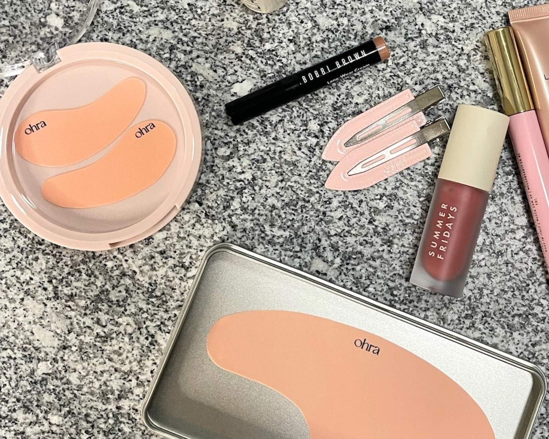 The Full Set flat lay, Self Made Eye Mask, Untouched Hair Clips, and Lifted Forehead Mask styled with makeup on granite