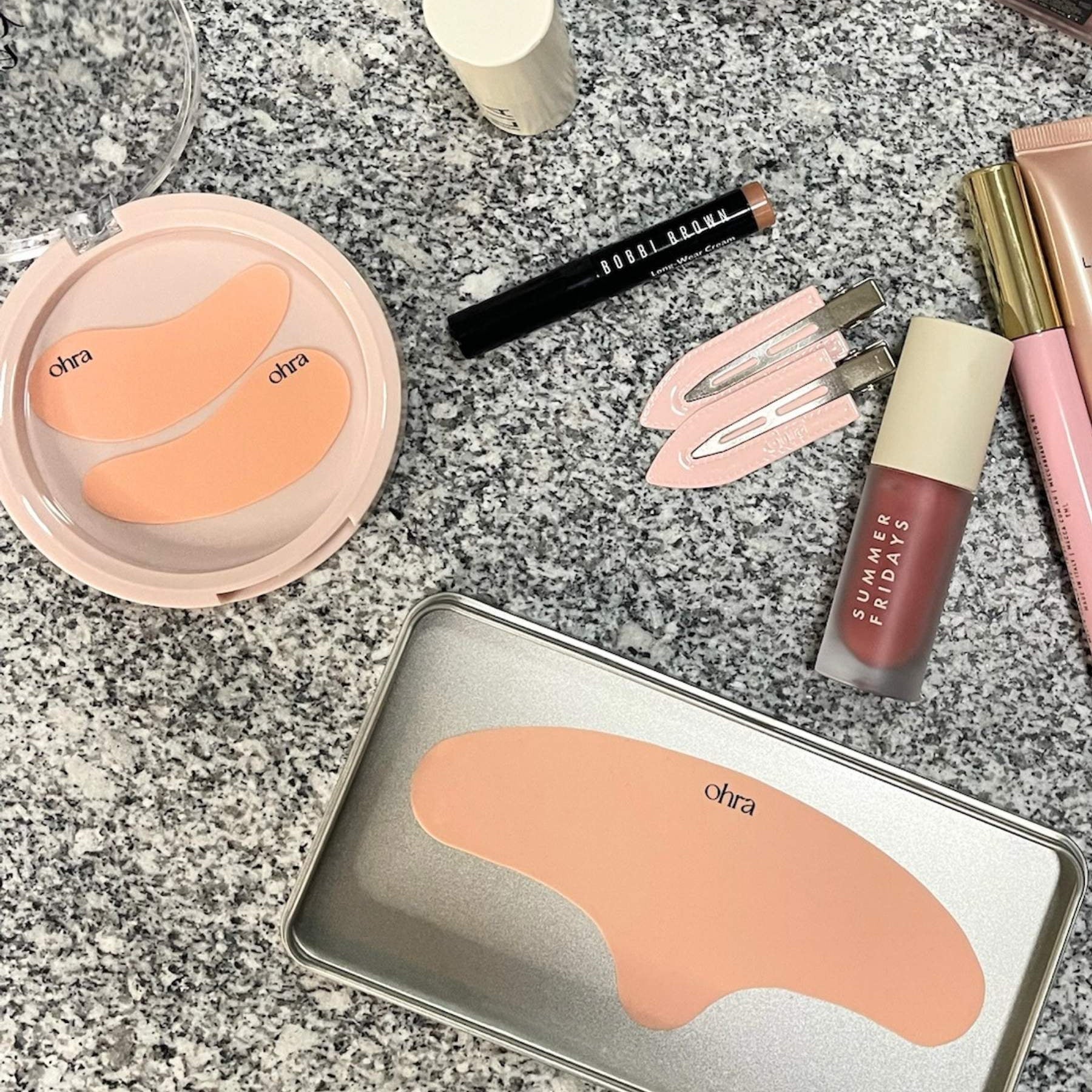 The Full Set flat lay, Self Made Eye Mask, Untouched Hair Clips, and Lifted Forehead Mask styled with makeup on granite