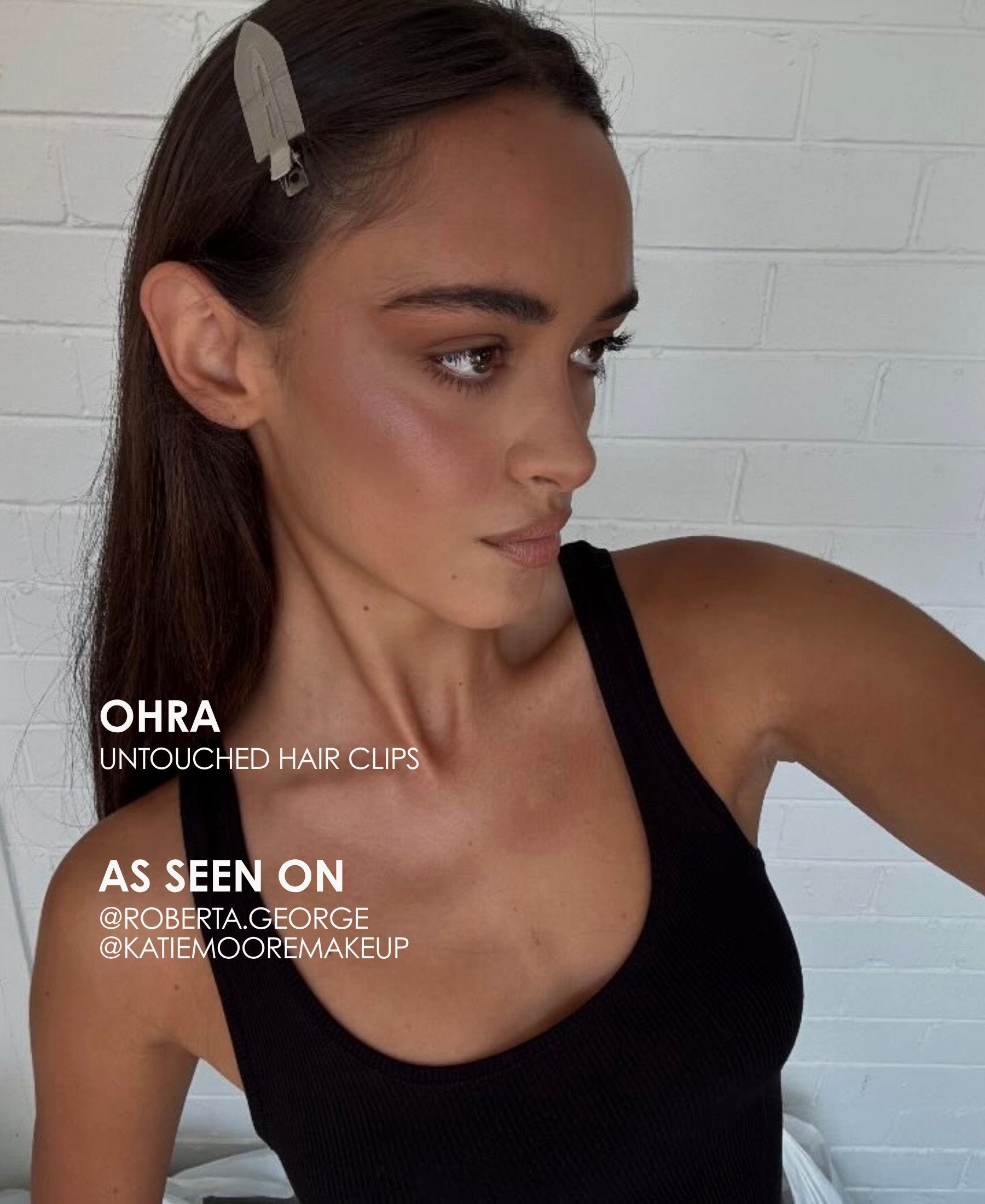 Woman wearing Ohra Untouched Hair Clips in her hair, styled with makeup during her application. A woman with long dark brown hair wearing a silver feather hair clip, shown in a close-up portrait against a white brick wall. Text on the image reads 'OHRA UNTOUCHED HAIR CLIPS'.