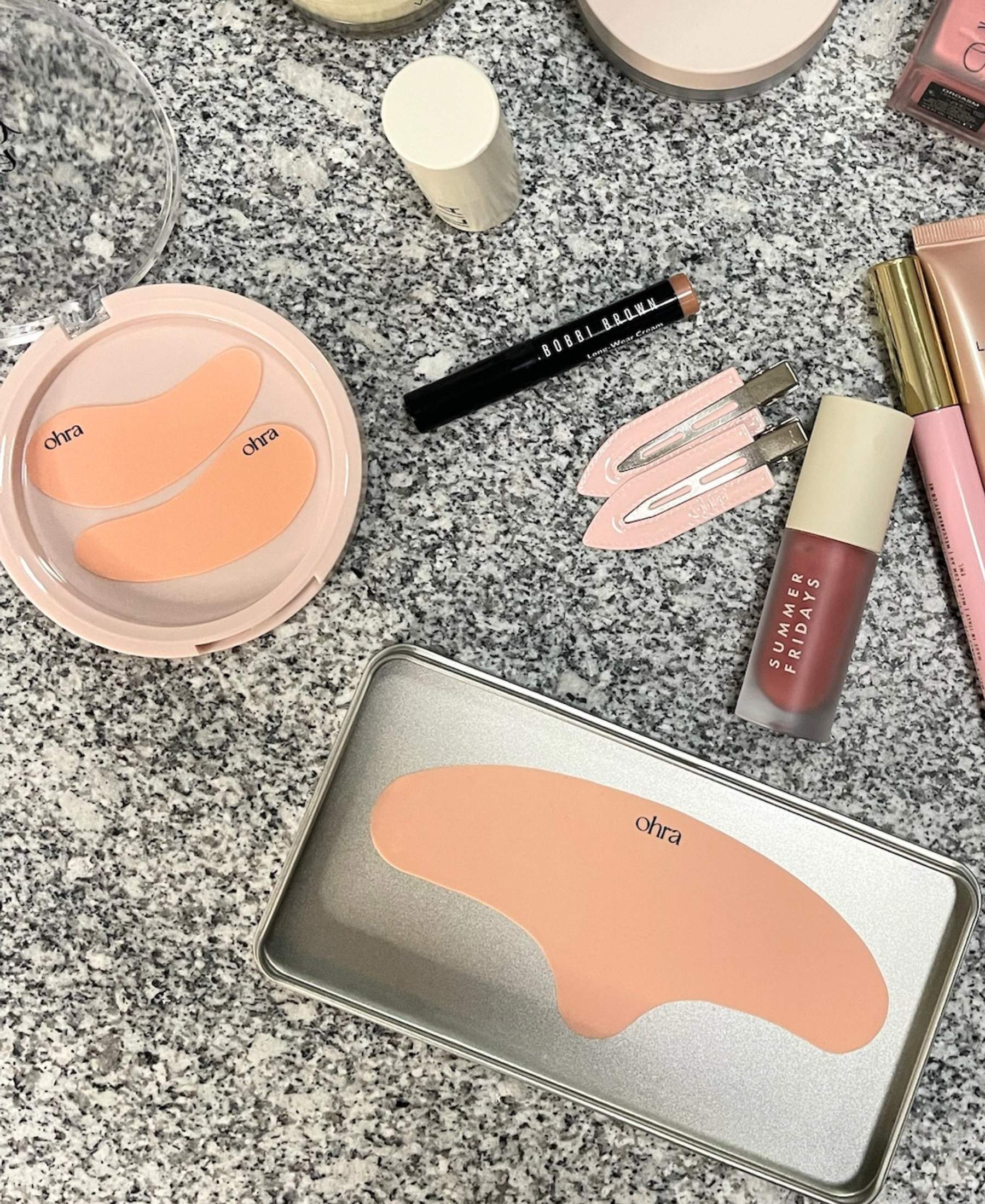 The Full Set flat lay, Self Made Eye Mask, Untouched Hair Clips, and Lifted Forehead Mask styled with makeup on granite